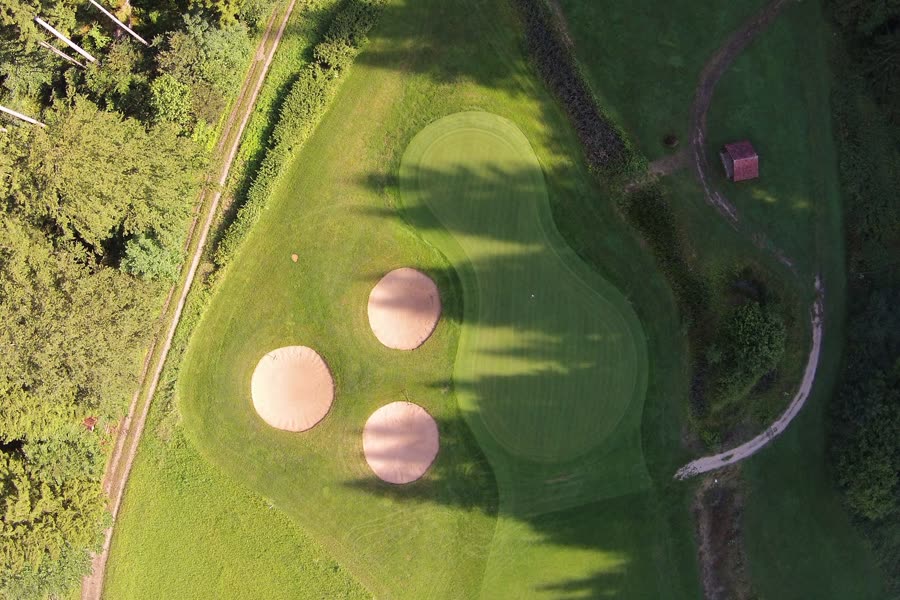 Senkrechte Drohnenaufnahme von Grün 13 mit drei Bunkern im Schatten hoher Bäume