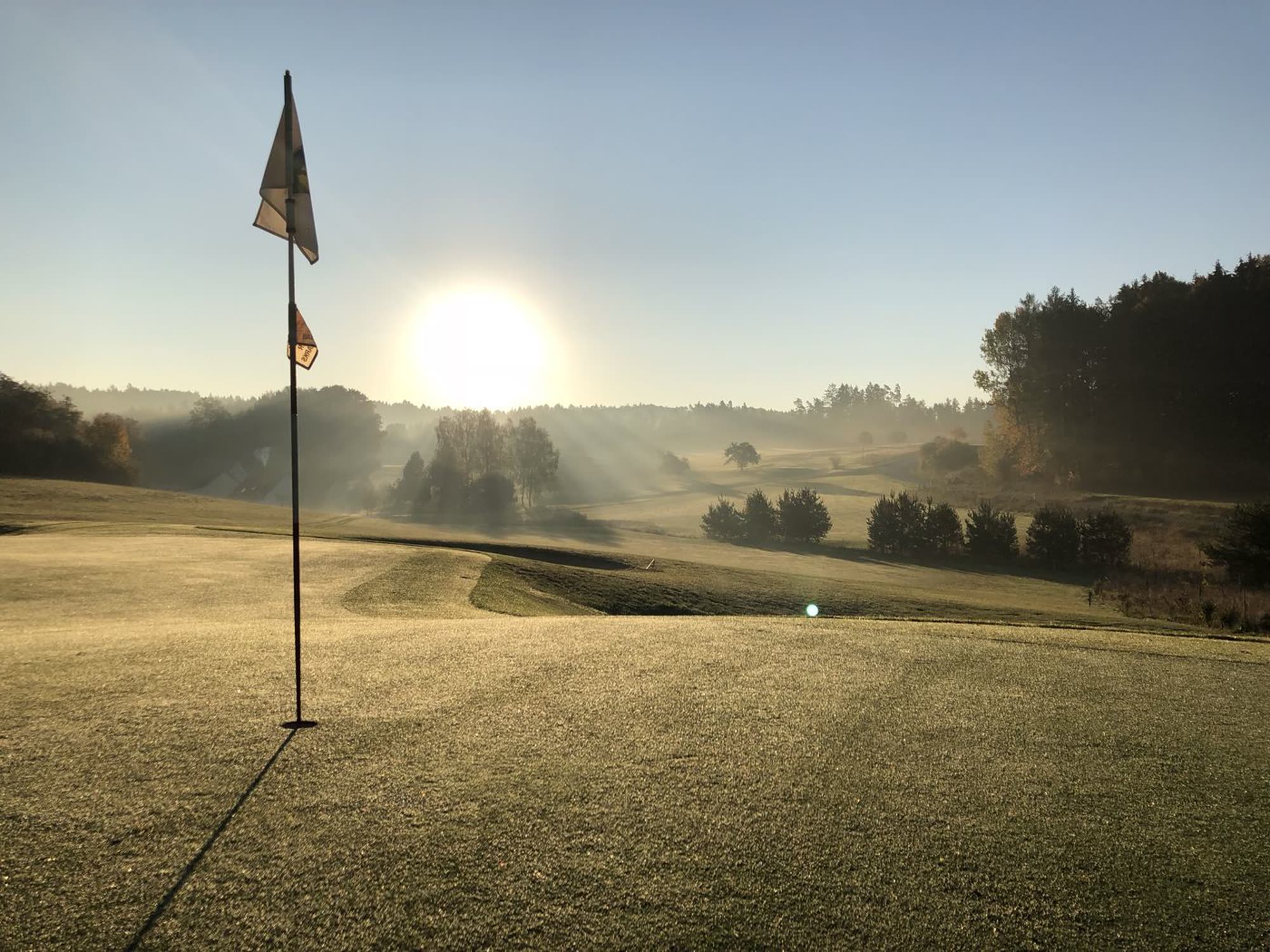 Morgennebel über Grün 9 der Golfanlage Gerhelm, die Fahne steht im Gegenlicht der aufgehenden Sonne