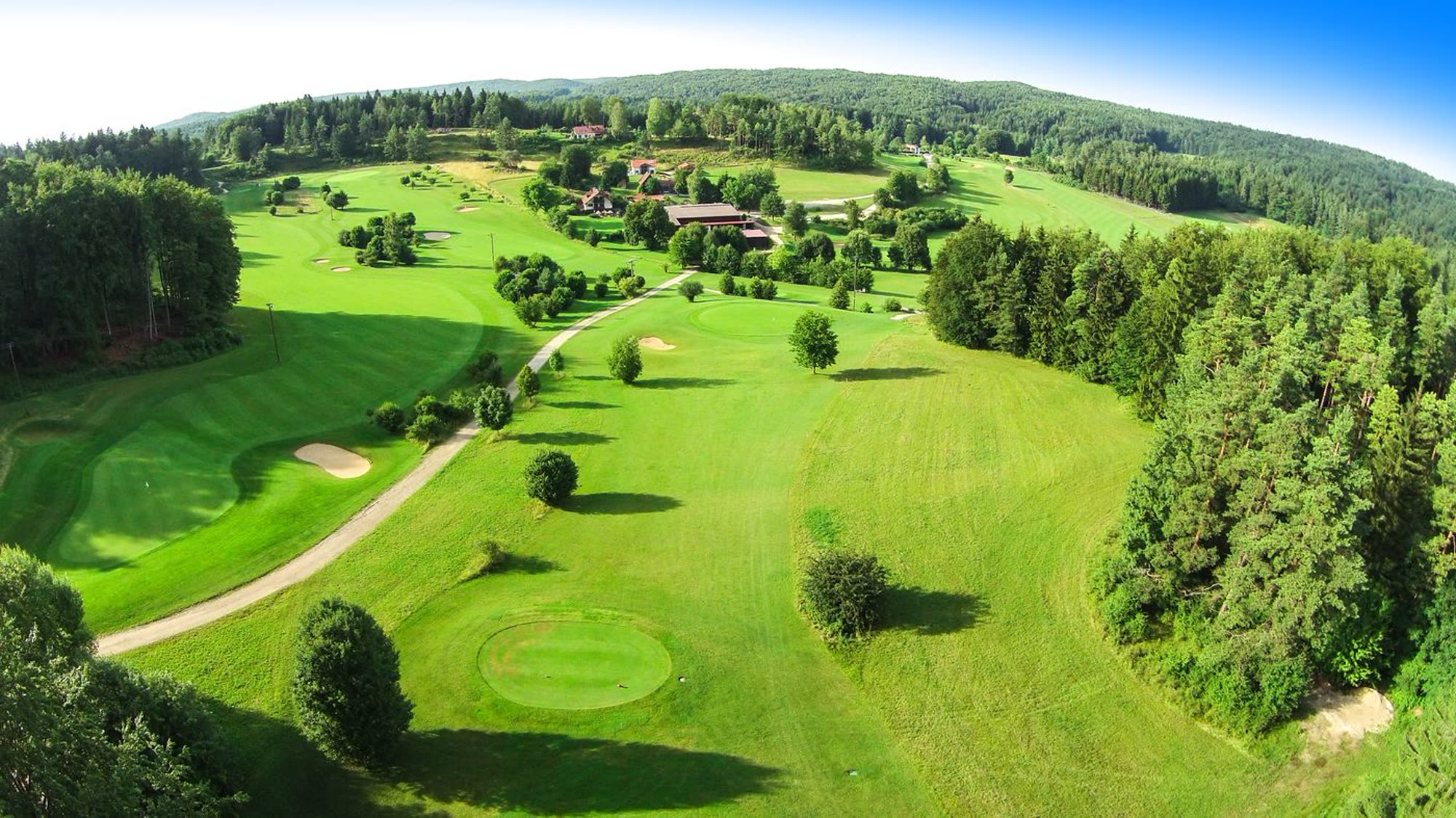Luftaufnahme der Golfanlage Gerhelm: Fairways und Grüns zwischen Wäldern, in der Mitte der Gutshof